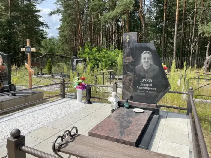 Памятник фигурной формы из тёмного гранита с золочёным крестом, кованой оградой и скульптурой ангела
